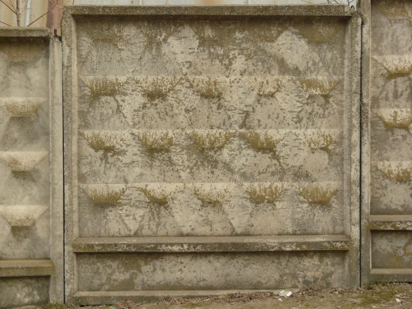 Concrete fence texture made up of rectangular slaps sloping upward, each with convex, white and grey square bricks. Patches of greenish-brown discoloration are visible throughout.